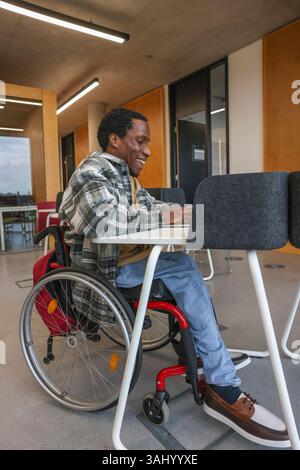 Man in wheelchair using laptop in office Stock Photo