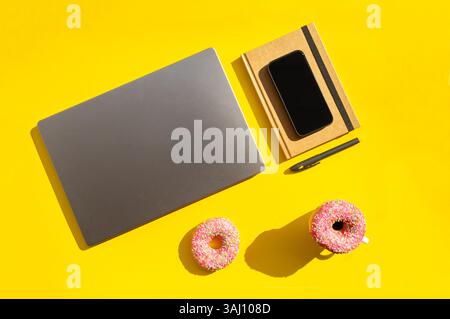 Creative Workspace with Donuts, Coffee and Laptop on Yellow Background Stock Photo
