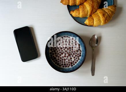 breakfast: cereal, chocolate balls with milk, croissants and smartphone on the table, flatlay Stock Photo