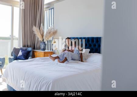 Happy mother and daughter posing in modern bedroom, with smartphone, bedding, decorative vase. Motherhood, portrait, connection, relaxation, lifestyle Stock Photo