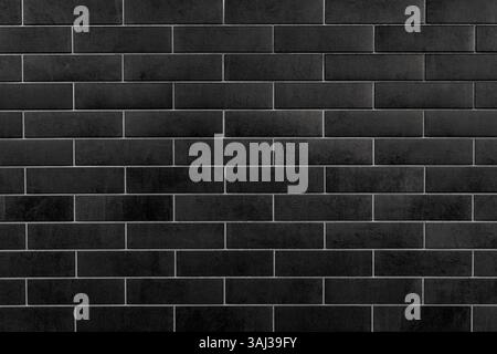 Black Rectangular Tiles Wall Background with Grid Pattern. A detailed view of a wall covered with black rectangular tiles arranged in a uniform grid Stock Photo