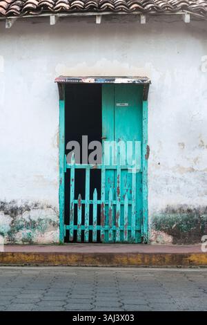 Unkempt turquoise colored wooden door with wicket in moldy white wall in a street in Nicaragua. Stock Photo