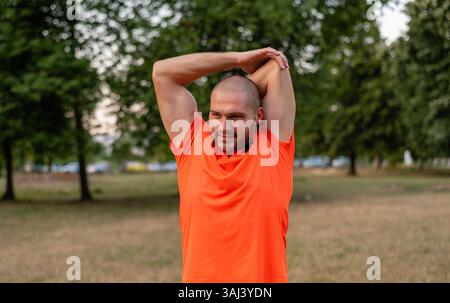 A sporty man is doing stretching exercises before running or workout outdoor in the summer park active healthy lifestyle.  Stock Photo