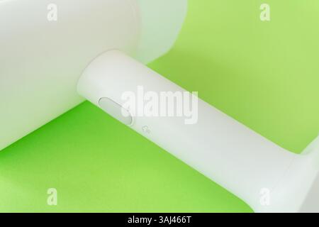 Close-up view of a white handheld steamer with a steam button,  resting on a vibrant green background. Stock Photo