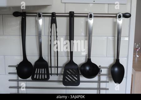 Different types of serving spoons hang on a rack on the kitchen wall Stock Photo