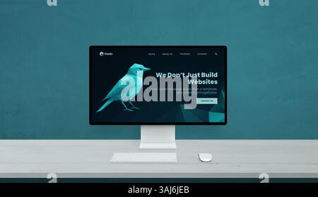 Desktop display featuring creative web agency design, polygon-style bird and tagline on blue interface, minimalist setup with white desk Stock Photo
