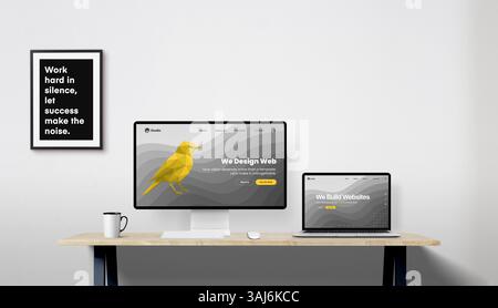 Desktop monitor and laptop on work desk displaying portfolio websites of a web design studio, picture frame on wall adds detail to the workspace Stock Photo