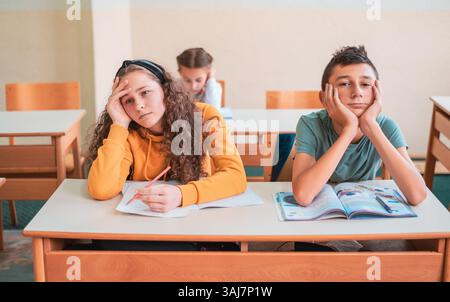 Tired and bored child students sitting in a school desk during the class. Stock Photo