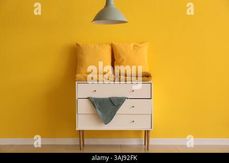 Pillows with folded blankets on commode near yellow wall in room Stock Photo