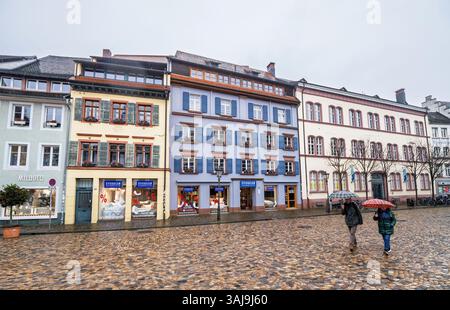 Freiburg, Germany - Feb 10, 2025: Colorful historic buildings with boutique stores and cobblestone pavement line a wet street in Freiburg as two pedes Stock Photo