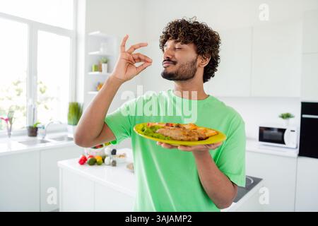 Young man enjoying homemade meal with delighted expression in modern bright kitchen filled with natural daylight Stock Photo