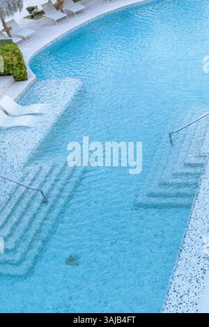 The serene pool features inviting crystal clear water and elegant steps leading down. A fun slide adds enjoyment, perfect for a relaxing day under the Stock Photo