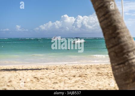Two boats float quietly on turquoise waters, with a sandy beach in the foreground and fluffy clouds scattered in a bright blue sky above. A peaceful c Stock Photo