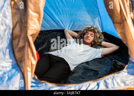 A young man lying with closed eyes in a camping tent. Happy sleeping. Stock Photo