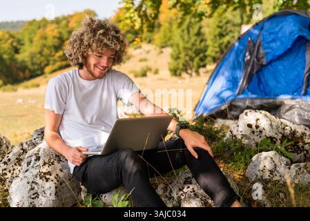 Young happy man freelancer working online using laptop in nature. Stock Photo