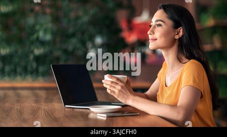 Happy young lady using laptop at cafe Stock Photo