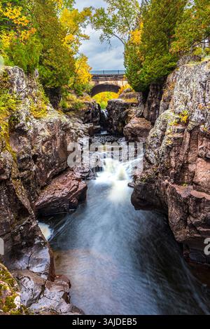 Majestic Autumn Waterfall Flowing Through Rocky Gorge Under a Stone Bridge Stock Photo