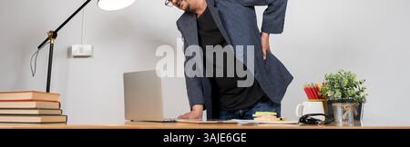 Millennial guy having health problem, bad posture due to sedentary work. Young businessman having acute back pain, massaging aching muscles, sitting a Stock Photo