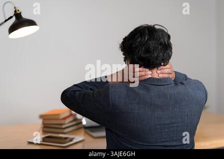 Neck ache concept. Young man sitting at office desk feeling hurt having pain in his neck. Man massage or rubbing stiff sore neck tensed muscles, fatig Stock Photo