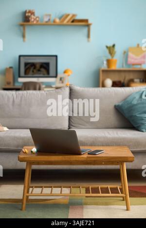 Modern living room with laptop on table, bookshelf and digital devices in background along with colorful decor, creating an inviting workspace Stock Photo