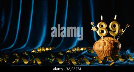 Number 89 gold celebration candle and small stars in sweet cupcake on bright blue velvet background. Concept of celebrating birthday, anniversary Stock Photo