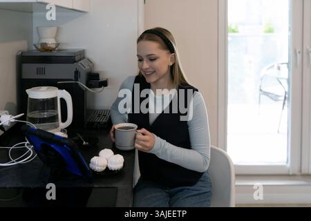 Woman enjoying coffee while using tablet at home kitchen in the morning hours Stock Photo