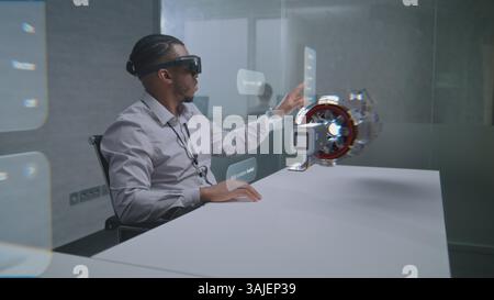 Futuristic Office: African American Professional Wearing Virtual Reality Headset to Visualize 3D Holographic Prototype of Green Energy Engine. Visualization of Artificial Intelligence Based Interface. Stock Photo