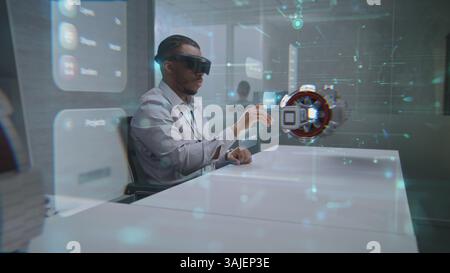 Futuristic Office: African American Professional Wearing Virtual Reality Headset to Visualize 3D Holographic Prototype of Green Energy Engine. Visualization of Artificial Intelligence Based Interface. Stock Photo