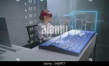Advanced Office: Female Professional Wearing VR Headset Uses Augmented Reality 3D Hologram to Visualize Wind Farm and Renewable Energy Transmission. Visualization of AI-based Software Interface. Stock Photo