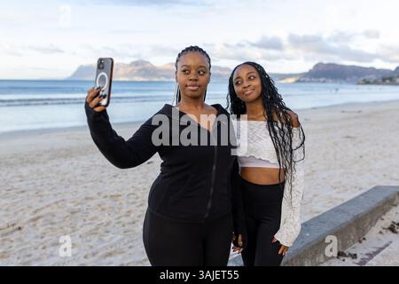 Young black females taking a selfie on the beach at sunrise Stock Photo