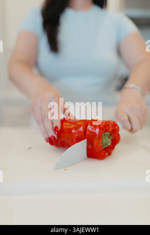 Woman slicing red bell pepper on white cutting board. Stock Photo