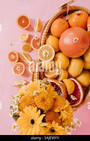Basket of citrus fruits and yellow flowers on pink background. Stock Photo