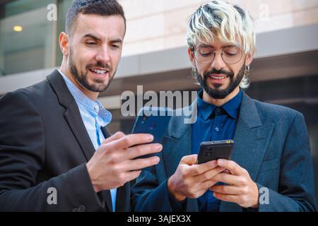 Two businessmen using smartphones outdoors in city, modern professional look Stock Photo