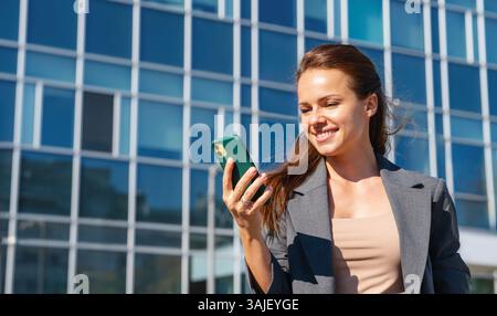 Successful businesswoman using smartphone outdoors in urban setting. Urban work-life balance. Stock Photo
