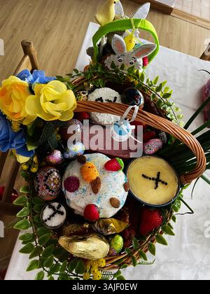 Easter basket with eggs, cakes, candles, and flowers arranged on a wooden table. Stock Photo