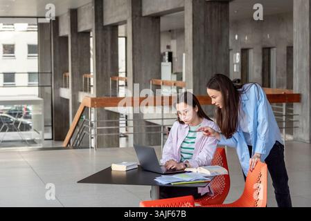 Two young women students work together on the laptop in the university lobby. Stock Photo