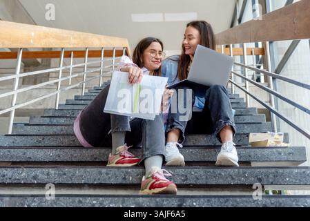 Low angle view with two female students sitting on the university stairs and preparing for exams Stock Photo