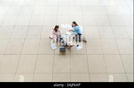 Above view with two students discussing and studying in the university lobby. Stock Photo