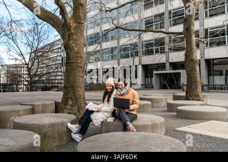 University students collaborate outdoors, laptops and books in hand on a crisp fall day Stock Photo