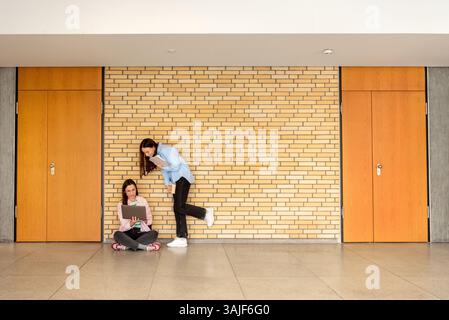 Two females students studying together using a laptop in the university lobby, in front of seminar rooms Stock Photo