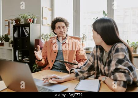 Medium shot of unrecognizable female developer looking at curly haired colleague while he telling about new project Stock Photo