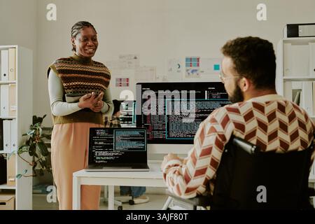 Back view of unrecognizable male IT specialist with disability having conversation with attractive African American colleague who standing in front of him Stock Photo