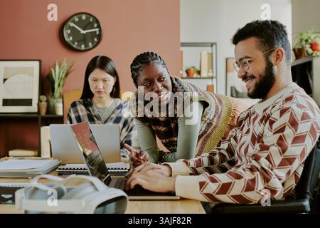Medium shot of male programmer typing and laughing while his adorable female African American colleague joking Stock Photo