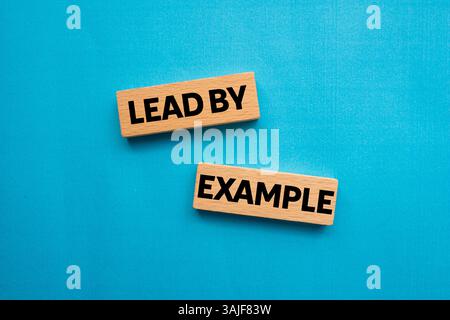 Lead by example message written on wooden blocks on blue background. Conceptual lead by example symbol. Copy space. Stock Photo
