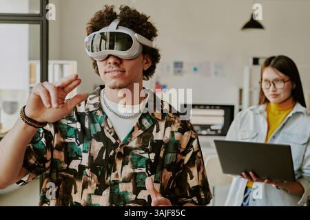 Medium shot of curly haired young man gesticulating in air while immersed into VR gaming Stock Photo
