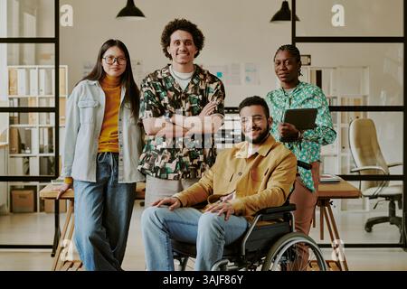 Medium full shot of biracial team dressed in casual clothes smiling at camera while working in cozy office Stock Photo