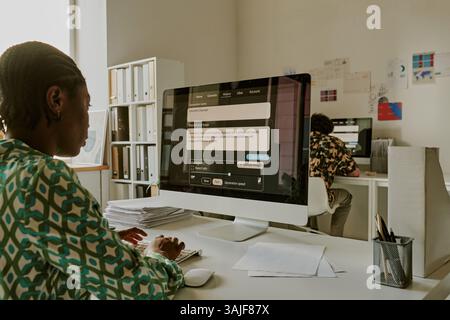 Unrecognizable African American woman texting with colleagues on social network discussing new project while working in office Stock Photo