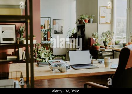 Spacious office with co-working zone equipped with desk, bookshelves and decorated with green plants in clay pots Stock Photo
