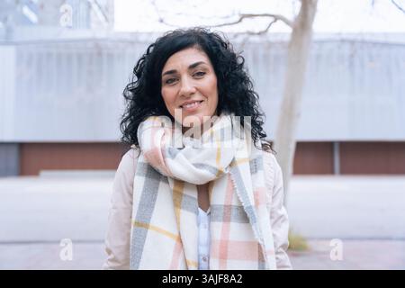 individual portrait Confident woman with curly black hair and scarf smiling  Stock Photo