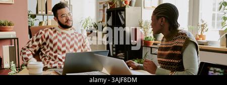 Website banner of two young colleagues having nice conversation while working on laptops during work day in office Stock Photo